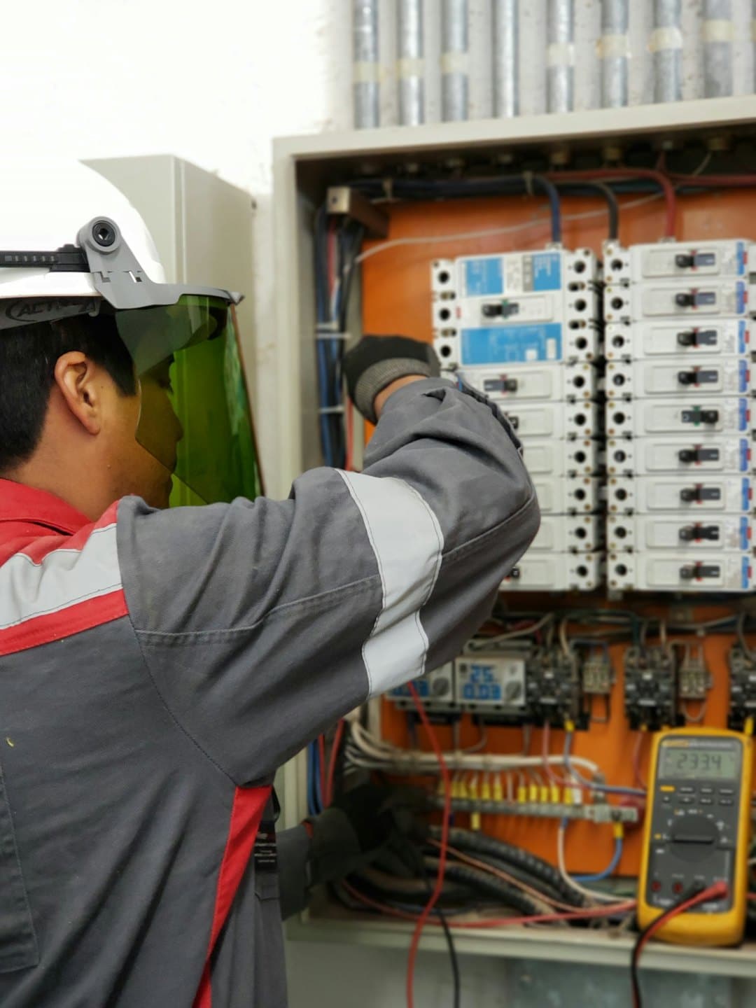 Technik kontroluje otvorený elektrický panel s ističmi a kabelážou.